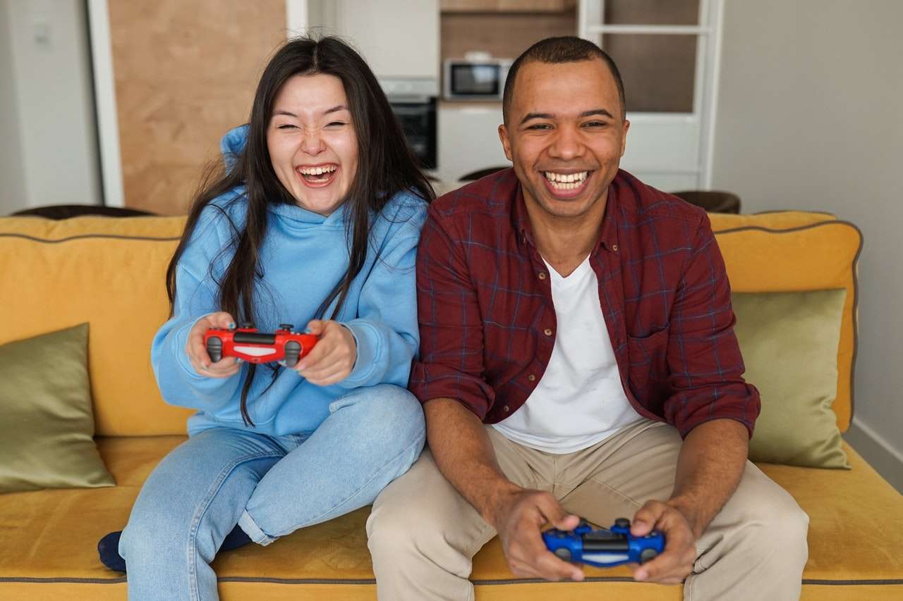 man and woman laughing happily while playing games with wireless game pads 